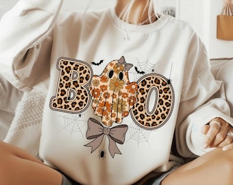 May include: White sweatshirt with a Halloween-themed design. The word "BOO" is spelled out with a leopard print "B" and "O", and a ghost with a floral design for the "O". Includes spiderwebs, bats, and a bow.