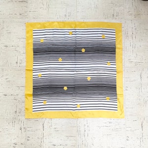 May include: A square scarf with a white and black striped pattern and gold-colored polka dots. The scarf has a gold border. This accessory can be worn around the neck or head.