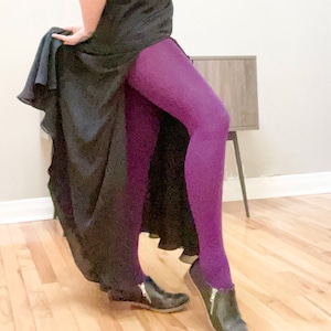May include: A pair of solid purple tights. The tights are worn with black ankle boots with zippers and a black dress. The dress is long and flowing.
