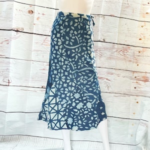 May include: A navy blue skirt with a white floral and geometric pattern. The skirt is knee-length and has a wrap-around design with a tie closure. The fabric is lightweight, suitable for warmer weather. The skirt's length is approximately 76 cm.