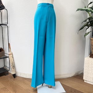 May include: Bright turquoise high-waisted pants with a button closure. The wide-leg trousers are displayed on a mannequin. The pants are made of a smooth, solid-colored fabric. The pants are a vibrant, eye-catching piece of clothing.