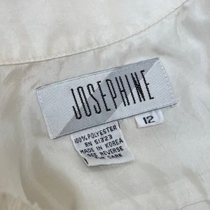 May include: Close-up of a white label with the name "JOSEPHINE" in black capital letters. The label also includes the size "12" and text indicating the material is 100% polyester and made in Korea.