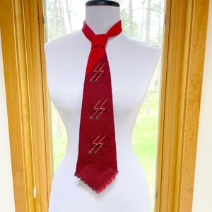 May include: A red tie with a lightning bolt design. The top portion of the tie is a solid red, transitioning to a darker red with three white and green lightning bolt designs. The tie is displayed on a white mannequin.