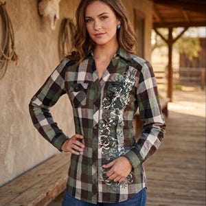 May include: A plaid button-down shirt in shades of green, brown, black, and white. The shirt features a floral design on the front and is paired with blue jeans. The long-sleeved shirt has a classic western style.