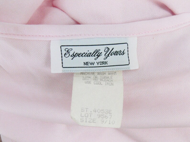 May include: Close-up of a light pink garment with a tag that reads "Especially Yours NEW YORK." The tag also includes washing instructions and size information. The garment is a soft, possibly knit, material.
