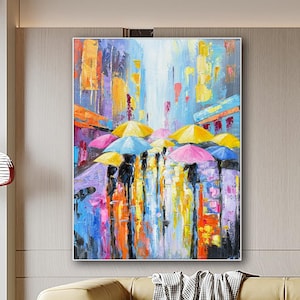 Könnte beinhalten: Ein rechteckiges Leinwandgemälde mit einer abstrakten Stadtstraßenszene im Regen. Das Kunstwerk zeigt leuchtend gelbe, rosa und blaue Regenschirme über dunklen Silhouetten mit dicken, strukturierten Farbstrichen in Orange, Violett und Weiß.