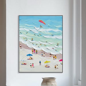 Puede incluir: Pintura enmarcada de una escena de playa, de estilo impasto. La obra representa una playa soleada con gente nadando, tomando el sol y bajo sombrillas de colores. Un parapente es visible en el cielo sobre las olas. La paleta de colores incluye azules, blancos y tonos arena.
