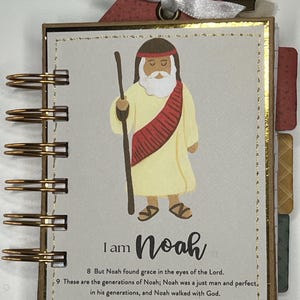 May include: A small, spiral-bound book with a gold-colored wire binding. The cover features an illustration of Noah holding a staff, with the text "I am Noah" and Bible verses. A decorative ribbon is attached at the top.