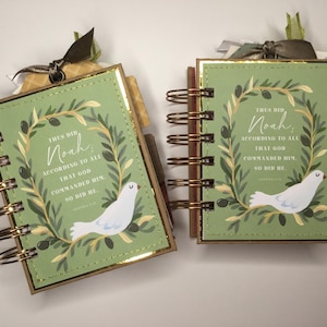 May include: Two small, spiral-bound notebooks with green covers and gold accents. Each notebook features a white dove illustration and text within a wreath design. The text reads "Thus did Noah, according to all that God commanded him, so did he."