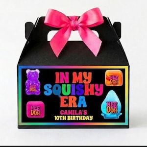 Puede incluir: Caja de regalo negra con un lazo rosa. La parte delantera presenta un diseño colorido con el texto "IN MY SQUISHY ERA" y "CAMILA'S 10TH BIRTHDAY". Incluye gráficos de ositos de goma y gotas de agua.