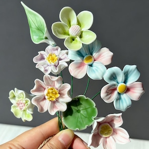 Könnte beinhalten: Ein Strauß aus Keramikblumen in verschiedenen Farben, darunter Rosa, Blau und Grün. Die Blumen haben gelbe Zentren und sind auf grünen Drahtstielen angeordnet. Der Strauß enthält Blätter.