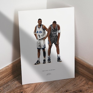 May include: A framed print featuring two basketball players in their team uniforms. One player is wearing a white and blue jersey with the number 1, and the other is in a black and white jersey with the number 32. The print has the text "Penny & Shaq // Orlando Magic".