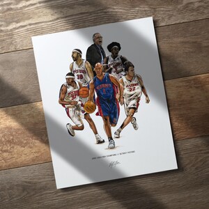 May include: A white art print featuring a detailed illustration of the 2003-2004 Detroit Pistons basketball team in action, including players in white and blue uniforms, a coach, and basketballs. Text reads 2003-2004 NBA CHAMPIONS // DETROIT PISTONS.