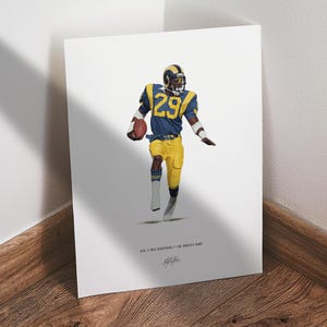 May include: A print featuring a football player in a blue and yellow uniform, number 29, holding a football. The player is wearing a helmet and is in motion. The print includes text at the bottom: "#29 // ERIC DICKERSON // LOS ANGELES RAMS".