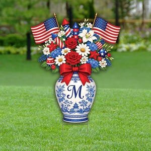 May include: A patriotic garden stake featuring a blue and white vase with the letter "M". The vase is filled with red, white, and blue flowers, American flags, and fireworks. A red bow adorns the vase.
