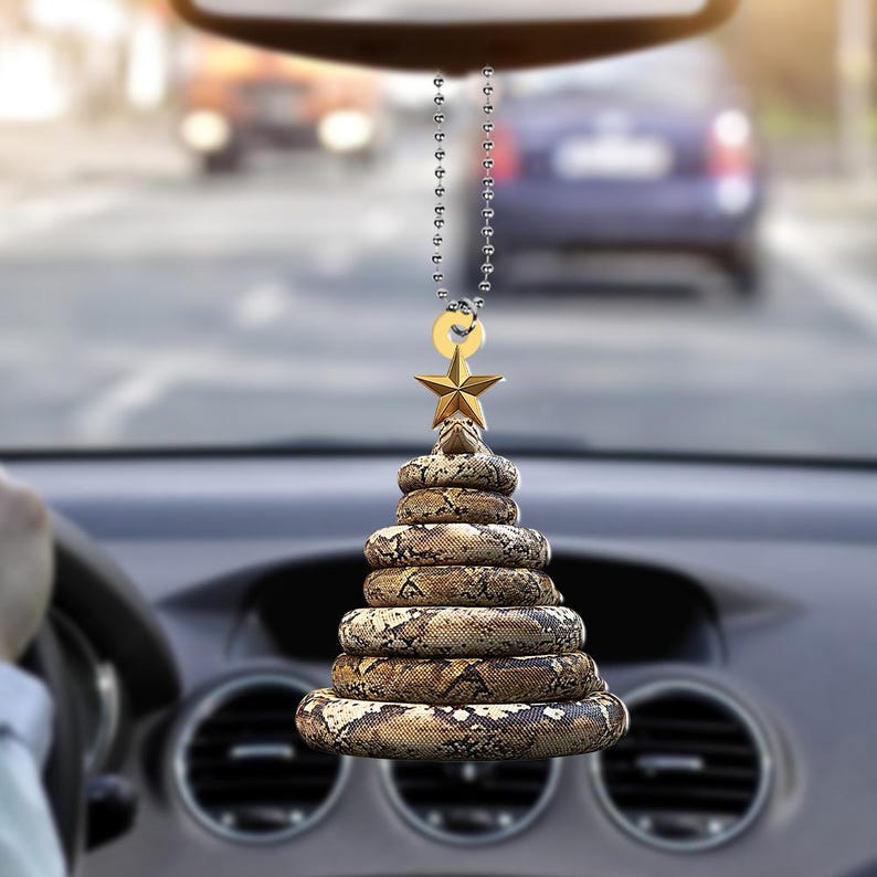 Pu&ograve; includere: Un profumatore per auto a forma di albero di Natale, realizzato con spirali impilate con un motivo a pelle di serpente. Una stella d'oro e un piccolo anello d'oro sono appesi a una catena d'argento. Il profumatore &egrave; appeso allo specchietto retrovisore di un'auto.