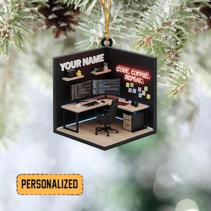 May include: A personalized ornament featuring a miniature computer workstation. The ornament includes a desk, chair, and dual monitors displaying code. The text "YOUR NAME" and "CODE COFFEE REPEAT" are visible. The ornament is suspended by a gold string.