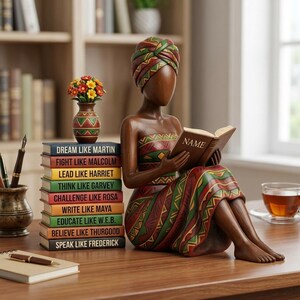 May include: A wooden figurine of a woman reading a book with the word "NAME" on the cover. She is wearing a patterned dress and head wrap. A stack of books with inspirational phrases and a small vase of flowers are next to her.