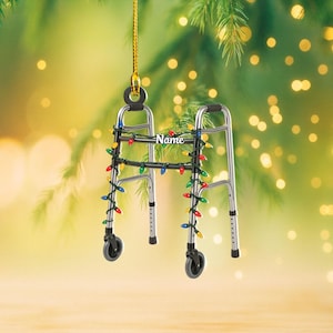 May include: A silver walker Christmas ornament decorated with colorful lights. The ornament has a black handle and wheels. The word "Name" is printed on the walker. The ornament is hanging from a gold string.