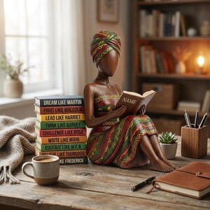 May include: A wooden figurine of a woman reading a book, with a stack of books beside her. The figurine is adorned in colorful patterns. The books have titles like "Dream Like Martin" and "Fight Like Malcolm". A mug and a notebook are also on the wooden table.