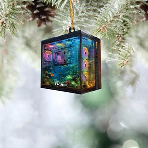 May include: A black, rectangular Christmas ornament shaped like a computer case. The ornament features a colorful aquarium scene inside, with fish and plants. The word "Name" is printed on the front. The ornament hangs from a gold string.