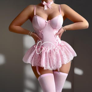 Könnte beinhalten: Hellrosa Dessous-Set mit einem Oberteil im Korsett-Stil, einem spitzenbesetzten Rock und passenden Strümpfen. Das Set enthält ein Halsband mit Schleife. Das Wort "Cosplay" ist auf der Vorderseite geschrieben.