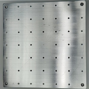 Op de afbeelding: Een vierkante zilverkleurige metalen plaat met een rasterpatroon, een centrale cirkelvormige geleider en gelijkmatig verdeelde gaten. Het oppervlak bevat gegraveerde hoekmarkeringen op 15, 30, 45, 60, 75 en 90 graden voor nauwkeurige uitlijning.