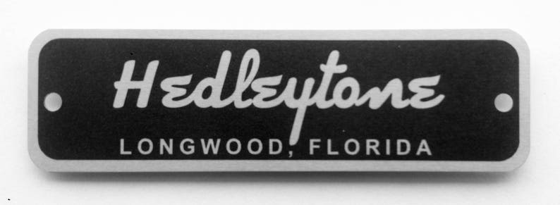 Puede incluir: Una placa de metal plateado con fondo negro. El texto "Hedleytone" est&aacute; escrito en una fuente blanca cursiva. Debajo del texto se encuentra la ubicaci&oacute;n "Longwood, Florida".