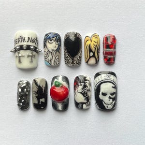 May include: A set of ten artificial nails with various designs. The designs include a skull, a heart, a red apple, and characters from the anime Death Note. The nails are painted in black, white, red, and yellow.