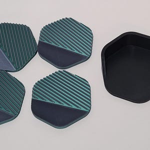 May include: A set of four teal and navy blue geometric coasters with a ribbed design, and a matching black hexagonal holder. The coasters have a two-tone color scheme and are designed to protect surfaces from drink condensation.