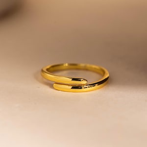 May include: A gold-colored ring with a wrap-around design. The ring is made of a shiny, reflective metal and has a smooth surface. The ring is a simple, elegant piece of jewelry.
