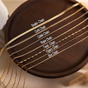 May include: A collection of seven gold-toned metal chains arranged in parallel, labelled as Snake Chain, Curb Chain, Cable Chain, Rope Chain, Twist Chain, Figaro Chain, and Box Chain. Each chain features a distinct link pattern and texture.