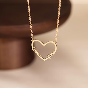 Puede incluir: Un collar dorado con un colgante en forma de corazón. El colgante lleva los nombres "Emma" y "Jane". El collar cuelga de una fina cadena, ofreciendo un diseño sencillo y elegante. Una joya delicada y encantadora.