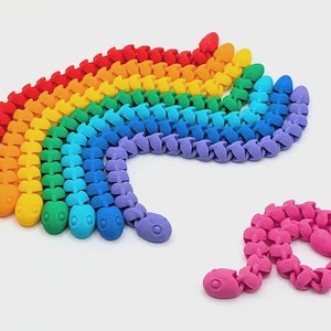 May include: A collection of articulated snake-shaped toys in a rainbow spectrum of colors including red, orange, yellow, green, blue, purple, and pink. Each snake features a segmented body design with a rounded head and visible eye details.