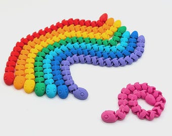 May include: A collection of articulated snake-shaped toys in a rainbow spectrum of colors including red, orange, yellow, green, blue, purple, and pink. Each snake features a segmented body design with a rounded head and visible eye details.