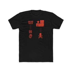 May include: Black t-shirt with a distressed red graphic design. The design includes the text "DREAM CREW", a star, a flag-like pattern, a grenade, the number "00", and a skull and crossbones. The shirt is made of a soft, comfortable material.