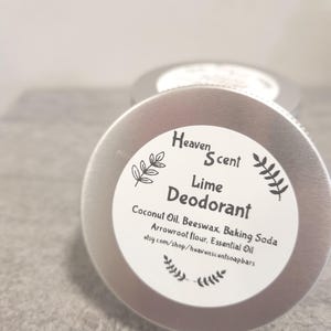 May include: Two silver metal containers of Lime Deodorant are shown in a close-up shot. The label on the front container reads "Heaven Scent Lime Deodorant" with the ingredients listed below. The background is a light grey surface.