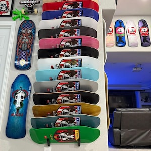 May include: A collection of skateboards in various colors, including black, red, and green, are displayed on a wall. Each board features a graphic of a bear with an American flag design. Additional skateboards and a framed skull artwork are also visible.
