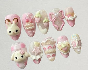 May include: A set of ten artificial nails in various designs. The nails are primarily pink and white, featuring 3D embellishments like a bunny, bow, strawberries, and cake. Some nails have a checkered pattern or heart accents.
