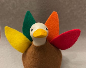 May include: A handcrafted turkey figurine with a brown felt body, a white head, and a yellow beak. The turkey's tail feathers are made of colorful felt in yellow, green, orange, and red. This Thanksgiving decoration is a charming addition to any festive display.
