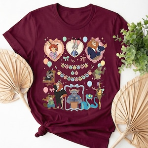 Puede incluir: Camiseta burdeos con un gr&aacute;fico colorido de personajes de Zootopia. El dise&ntilde;o incluye retratos enmarcados, globos y el texto "Welcome to Zootopia". La camiseta est&aacute; anudada en la parte inferior.