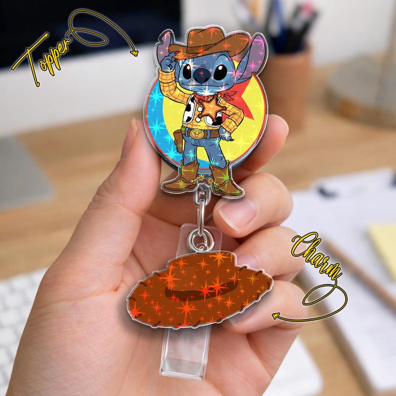 May include: A badge reel featuring a cartoon character dressed as a cowboy. The character is blue with large ears, wearing a brown hat, yellow shirt, and blue pants. The reel has a matching cowboy hat charm.