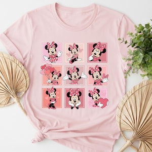 May include: Pale pink t-shirt with a grid of nine Minnie Mouse illustrations. Each Minnie Mouse is depicted in a different pose, wearing a pink dress and bow. The shirt is made of a soft material.