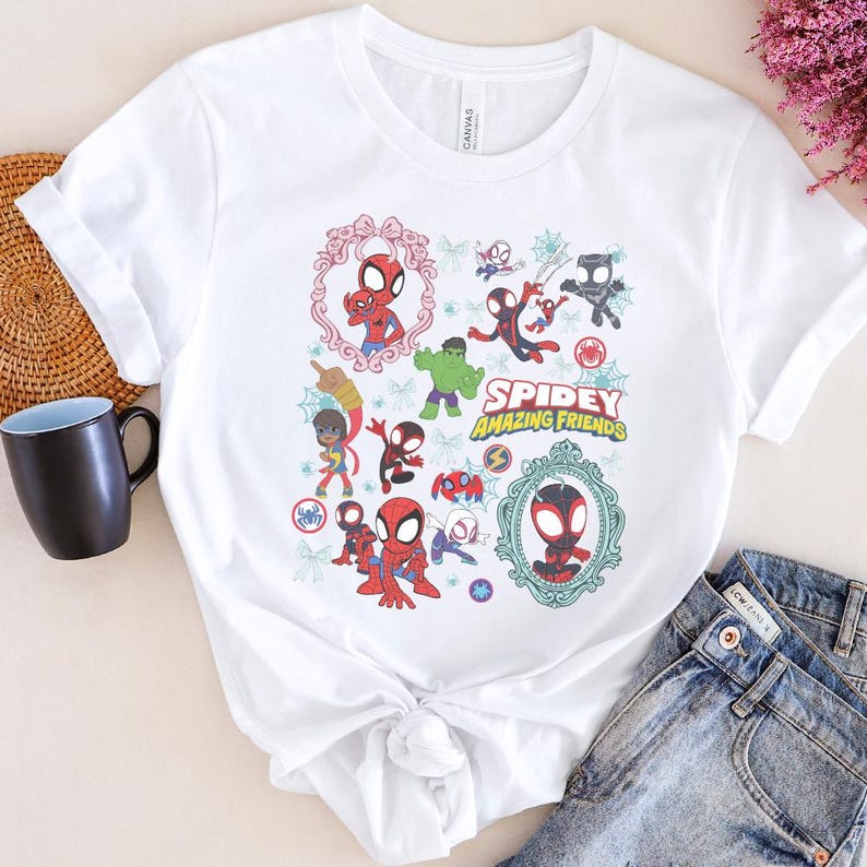 May include: White t-shirt featuring a colorful graphic of Spider-Man and other characters from the "Spidey and His Amazing Friends" animated series. The design includes the show's title and various illustrations of the characters in action poses.