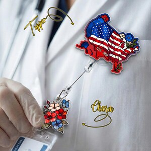 May include: A badge reel with a United States map design featuring the American flag and the text "1776-2026." The reel also includes a floral charm with red, blue, and peach-colored flowers.