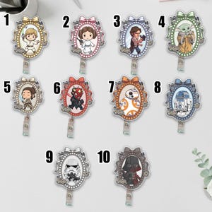 May include: A collection of ten Star Wars themed badge reels. Each reel features a different character illustration within an oval frame, adorned with a decorative bow. The characters include Luke Skywalker, Princess Leia, Han Solo, Grogu, Rey, Darth Maul, BB-8, R2-D2, a Stormtrooper, and Darth Vader.