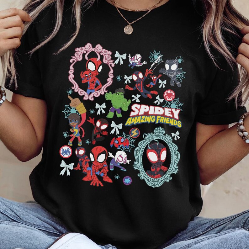May include: Black t-shirt featuring a colorful graphic of Spider-Man and friends. The design includes various characters, spiderwebs, and the text "Spidey Amazing Friends" in yellow and white.