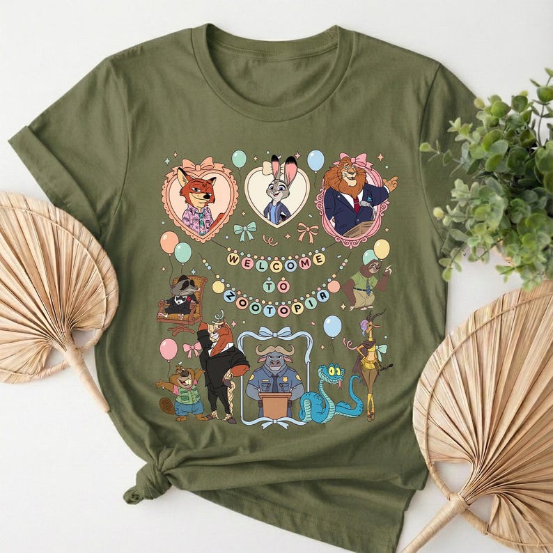 Puede incluir: Camiseta verde oliva con un gr&aacute;fico colorido de personajes de la pel&iacute;cula Zootopia. El dise&ntilde;o incluye el texto "WELCOME TO ZOOTOPIA" y varios personajes de animales en marcos con forma de coraz&oacute;n y otros elementos decorativos.