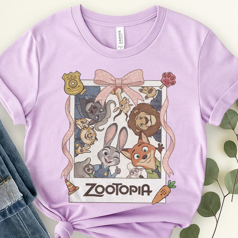 K&ouml;nnte beinhalten: Helllila T-Shirt mit einem Zootopia-Film-Motiv. Das Design zeigt ein Bild im Polaroid-Stil mit Charakteren wie Judy Hopps und Nick Wilde, eine rosa Schleife und das Wort "Zootopia".