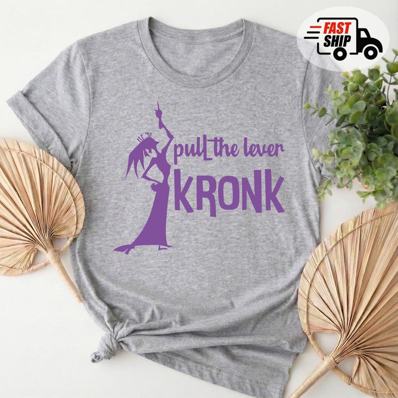 May include: A heather gray t-shirt featuring a purple graphic of a character and the text "pull the lever KRONK". The design includes a silhouette of a character in a dramatic pose. The shirt is made of a soft material.